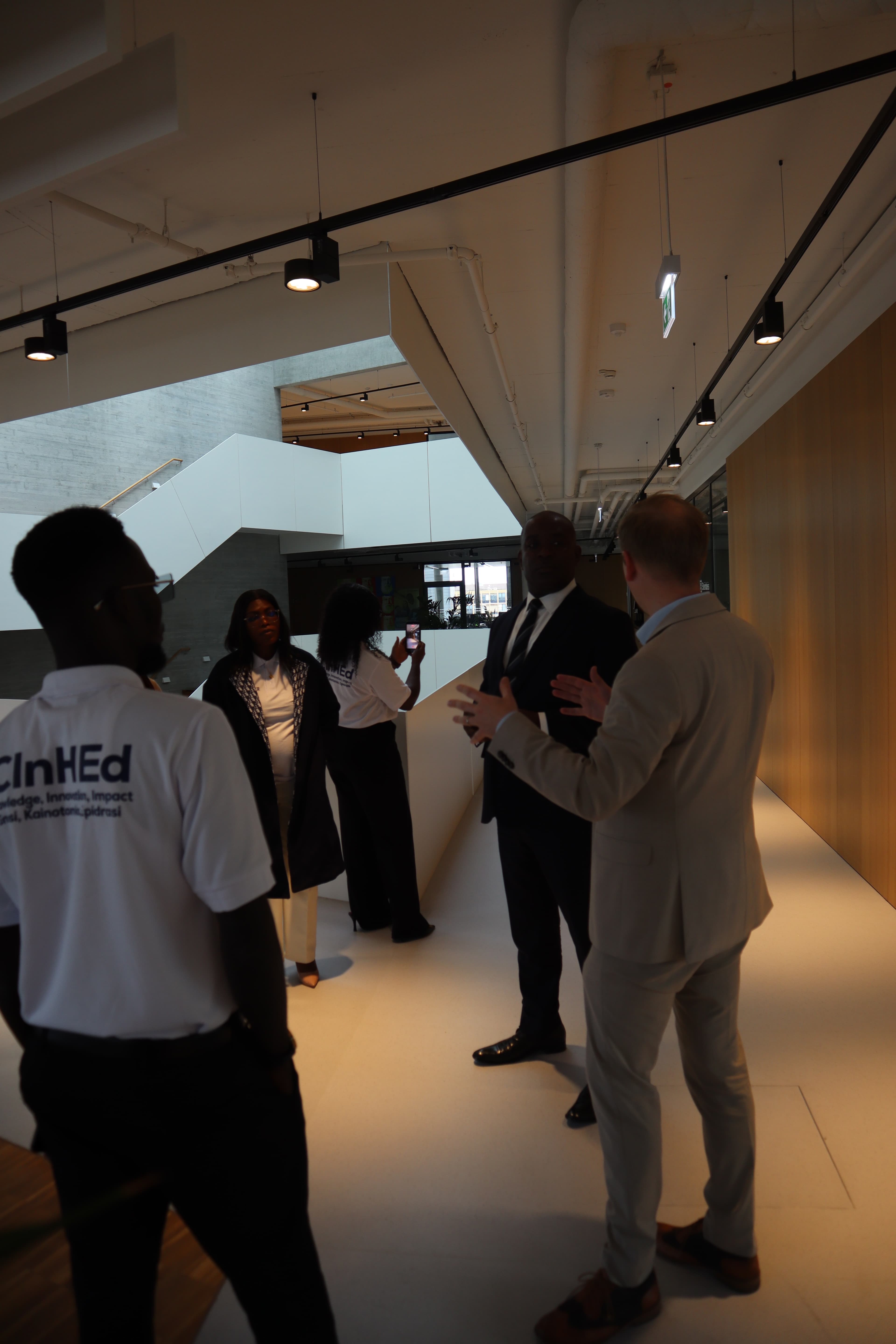 Delegation members gather around a speaker in a hallway, including a participant wearing a CInHEd shirt.